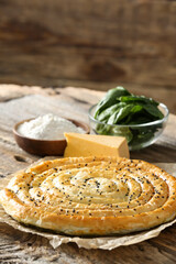 Tasty spinach pie and ingredients on wooden background