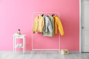 Rack with stylish jackets near pink wall in hallway
