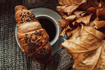 A cup of black morning coffee with a chocolate croissant in a cozy autumnal still life. Delicious meal. Aesthetics in details