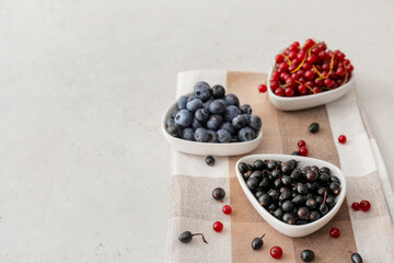 Bowls with different ripe berries on light background