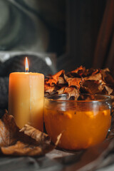 Burning candle and a large mug of hot orange sea buckthorn tea in a cozy home autumn evening still life with dry leaves.