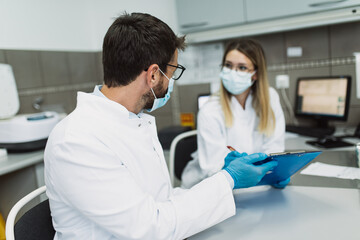 Two scientists or technicians with face protective masks work in laboratory on human blood samples.