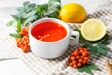 Cup of tasty rowan tea, berries and lemon on table
