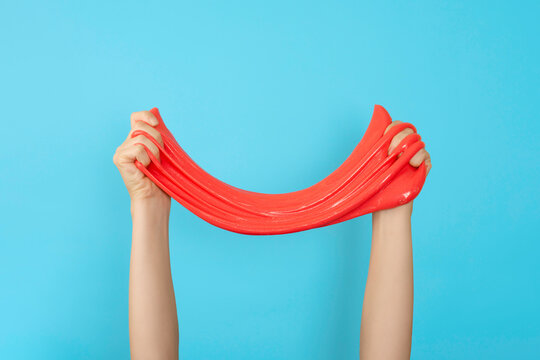 Close up on shiny red or coral slime in the hand isolated on blue background. Fun and stress relief concept