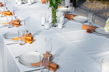 Wedding table setting decorated with fresh flowers in a brass vase. Wedding floristry. Banquet table for guests outdoors with a view of green nature. Bouquet with roses