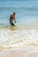 A well built young sexy black guy, half naked,  is walking on water of ocean, turning around, looking at you..