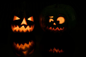 Halloween pumpkin smile and scary eyes for party night with reflection. Close up view of scary Halloween pumpkin with eyes glowing inside at dark background. Selective focus