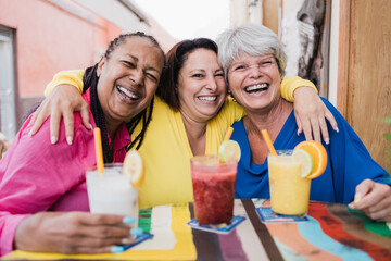 Multiracial senior woman having fun drinking healthy smoothies at brunch restaurant - Focus on...