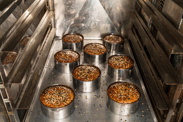 Raw of small bread buns decorated with seeds into an oven