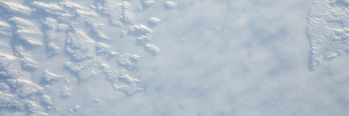 Beautiful winter background with snowy ground. Natural snow texture. Wind sculpted patterns on snow surface. Wide panoramic texture for background and design.