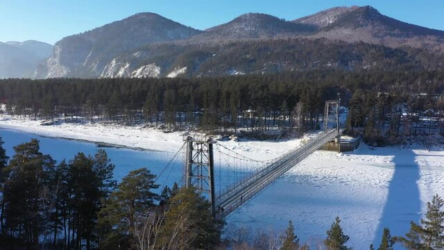Aerial footage of scenery bridge over frozen river in winter. Nature of Altai Republic. River Katun covered by snow and mountains on background