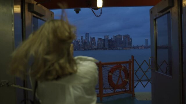 A female looks off into the distance, deep in thought while staring at the New York City skyline while riding the Staten Island Ferry. Back view of tourist on Staten Island Ferry approaching Manhattan