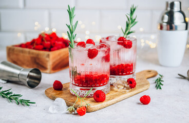 Raspberry lemonade in a glass with ice and fresh rosemary on a stone background.