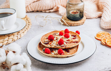 Fresh homemade pancakes with almonds, raspberry and coffee on white kithen background. Cozy breakfast