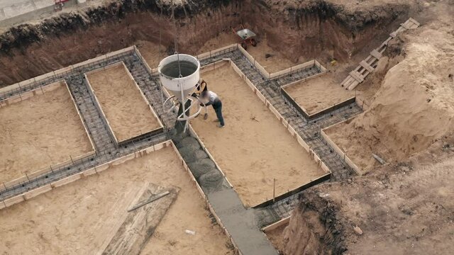 Construction site with workers pouring concrete in formwork with reinforcement. Wet cement pours to civil building foundation, aerial view.