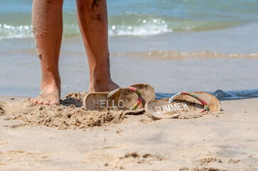 Sandy legs and flip flops on the beach with te words Hello Summer