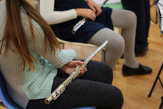 Girl student with a musical instrument flute sitting in the hall at the rehearsal of the school orchestra.Child hobby leisure learning music background image in informal clothes free pose close-up