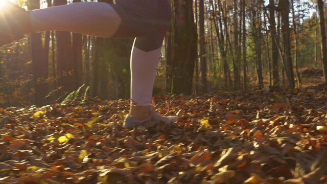 SLOW MOTION, LOW ANGLE, CLOSE UP, LENS FLARE: Unrecognizable fit woman jogs along a forest trail illuminated by the setting sun. Cinematic shot of a female jogger exploring the autumn colored woods.