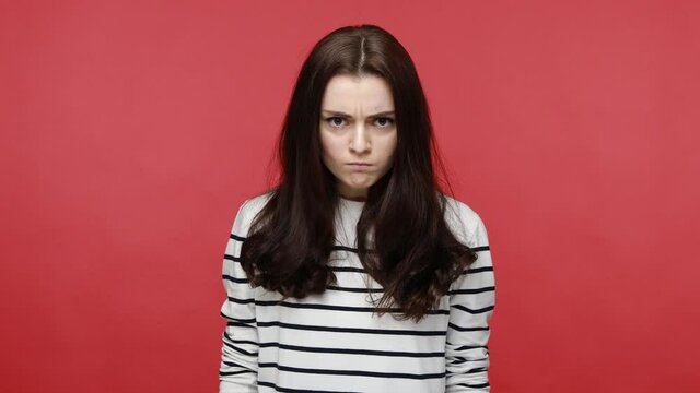 Portrait of angry woman looks at camera, expressing negative aggressive emotions, being in bad mood, wearing casual style long sleeve shirt. Indoor studio shot isolated on red background.