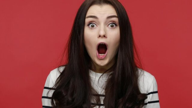 Portrait of surprised woman standing open mouth, hearing astonishing news, saying wow with shock, wearing casual style long sleeve shirt. Indoor studio shot isolated on red background.