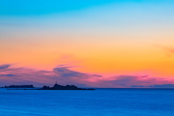 Silhouettes of buildings on the island against the colorful sea horizon.