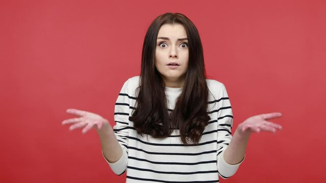 Portrait of young woman raising hands in anger and shouting why how, what do you want, quarreling, wearing casual style long sleeve shirt. Indoor studio shot isolated on red background.