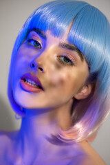 Beautiful young woman in pink and blue wig with clean perfect skin and makeup in neon studio light with light and shadows in her skin. Selective focus. Portrait of beauty model with long eyelashes.