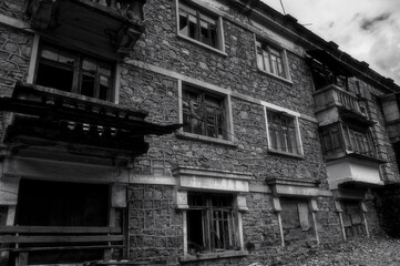 Black and white photo of old abandoned partially collapsed building with intricate stonework, ruined balconies, crashed windows. Desolation and destruction