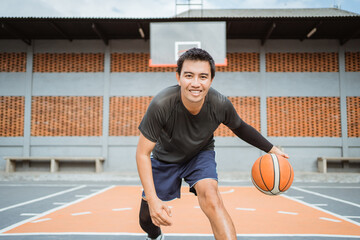 a smiling male basketball player doing a low dribble between the legs dribble with the ball