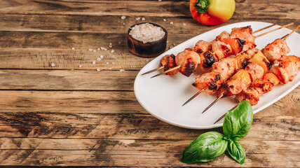 Grilled chicken on bamboo skewers with basil on rustic wooden background.