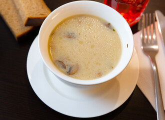 Portion of fresh mushroom soup served in soup bowl with serving pieces and brea