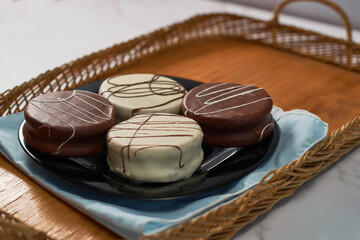 Traditional white and brown chocolate alfajores on a rustic wooden tray.