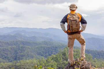 Young hiker male with backpack relaxing standing on top of a mountain and enjoying the view of valley