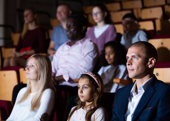 Obraz premium Father, mom and daughter are carefully watching spectacle or concert in the theater auditorium