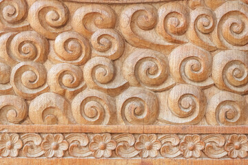 Pattern of flower and coiled spiral carved on teak wood background.