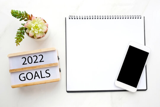2022 goals on wood box and blank notebook paper on white marble background, business new year aim to success