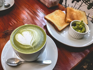 Afternoon tea date in couple with delicious big cup of matcha latte with a heart (japanese green matcha tea and milk) and toast with smashed avocado 