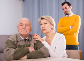 Man seriously talking with his mature mother and aged father at home