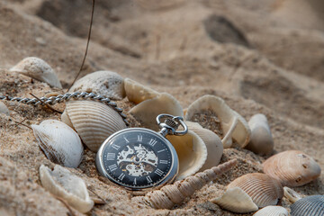Antique pocket watch and shells in sand on the beach and copy space. Time of life in nature...