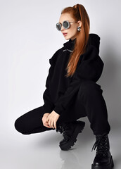 Slim fashionable redhead woman grunge and rock star in round sunglasses trendy black sportswear...