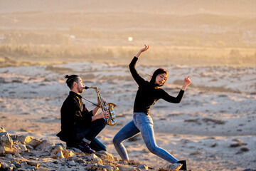 latin musician is playing saxophone while latin woman is dancing in the desert landscape