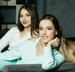 Two smiling friends sitting on the couch looking at camera in sitting room at home