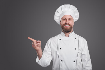 Smiling chef pointing away on gray background