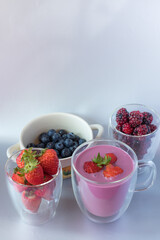a delicious and healthy sugar-free diet yogurt served in a clear glass cup with strawberries with blueberries and blackberries on a gray background