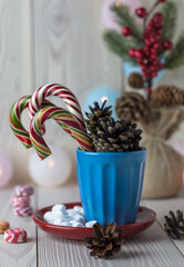 traditional festive christmas still life closeup, colorful candy canes and cones in the blue cup on white wooden background 