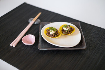 Asian style meat tartlets on white plate with wooden chopsticks on black mat in Japanese restaurant. close up, photo for the menu