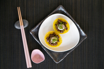 Asian style meat tartlets on white plate with wooden chopsticks on black mat in Japanese restaurant. close up, photo for the menu