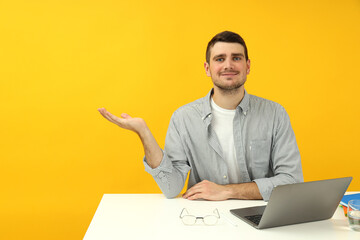 Study concept with young man sitting on the table on yellow background