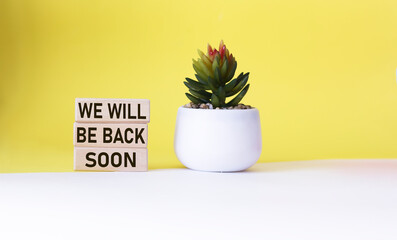 WE WILL BE BACK SOON text on wooden blocks and white and yellow background with cactus.