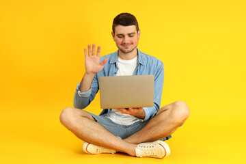Young man talking on video communication on laptop on yellow background